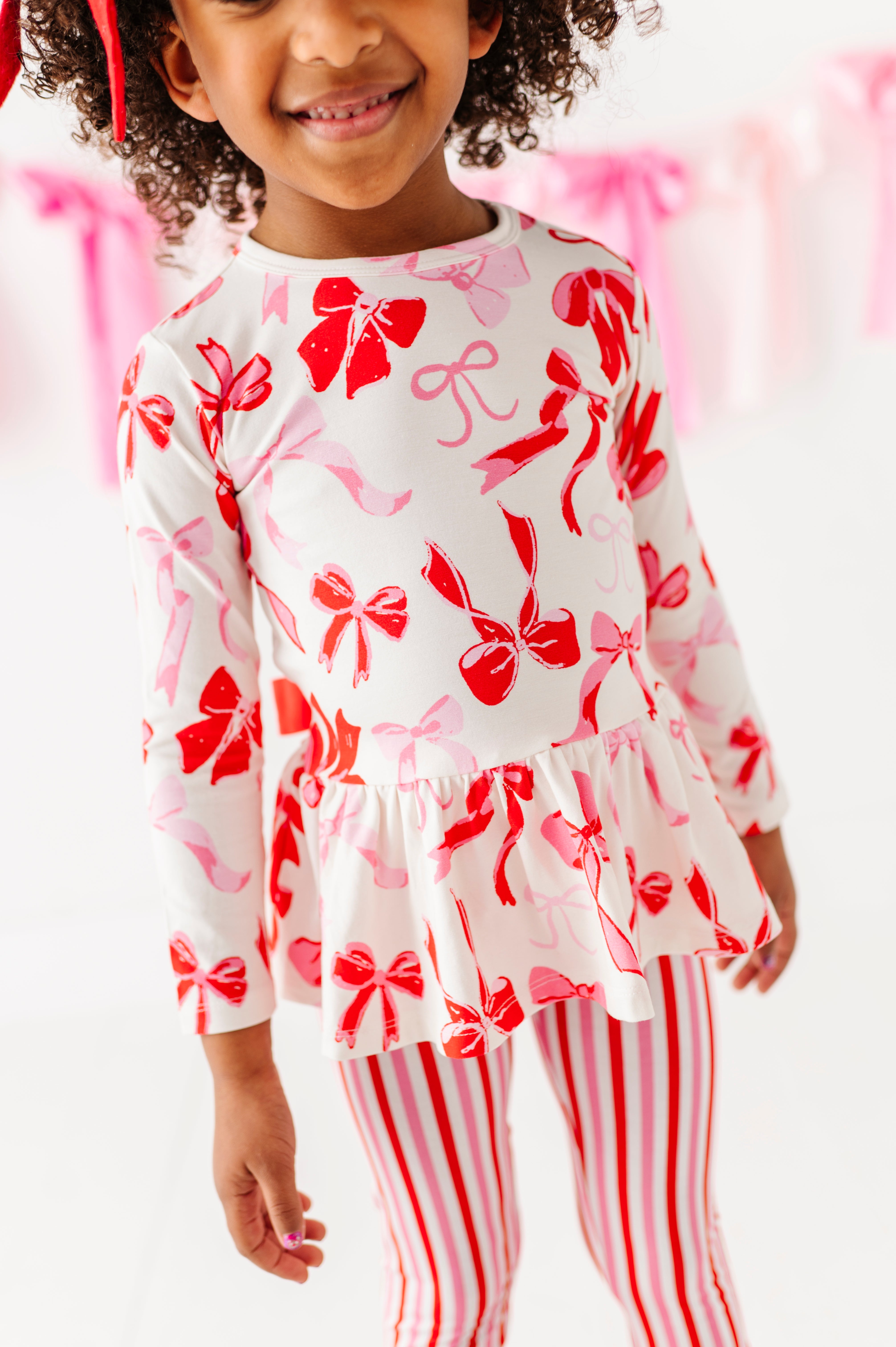 Girl standing in Blushing Bows peplum top and pink striped bottoms